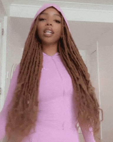 a woman with long dreadlocks is wearing a pink hoodie .