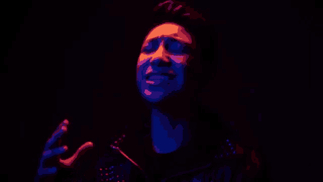 a close up of a man 's face in a dark room with a blue and red light behind him .