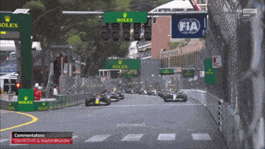 a row of racing cars are lined up on a track with a rolex sign in the background