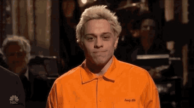 a man with blonde hair is wearing an orange shirt .