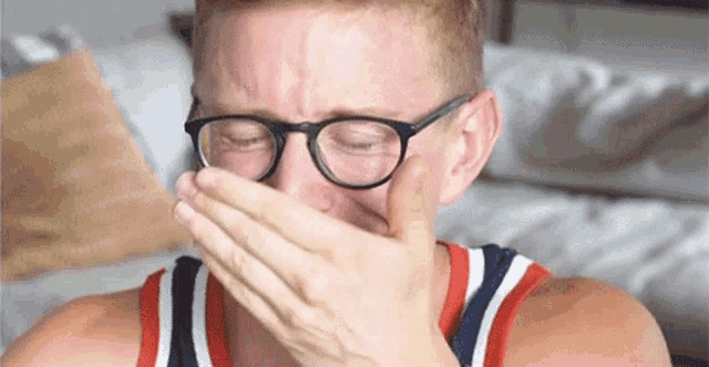 a man with glasses is covering his mouth with his hand .