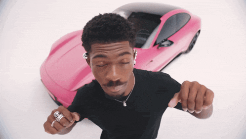 a man is dancing in front of a pink sports car