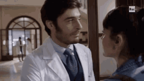a man in a lab coat and tie is kissing a woman in a hospital .