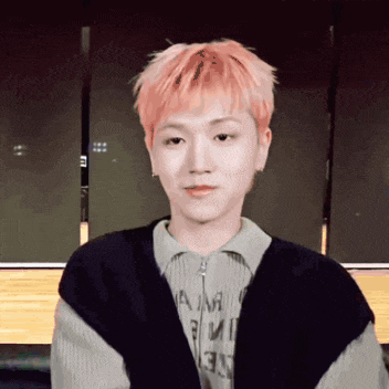 a young man with pink hair is wearing a sweater that says am