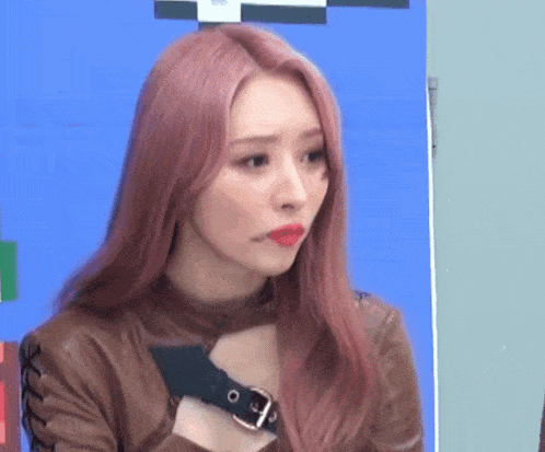 a woman with pink hair and red lipstick is wearing a brown leather jacket and a black belt around her neck .