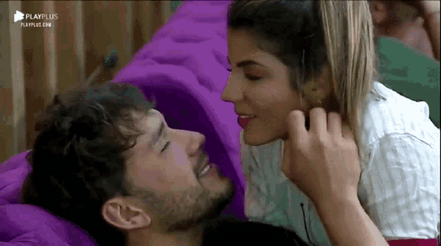 a woman is kissing a man on the cheek while laying on a bed with a playplus logo on the bottom