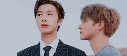 two young men are standing next to each other and one is wearing a suit and tie .