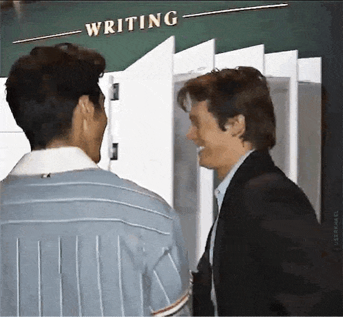 two men are standing next to each other in front of a chalkboard that says writing .