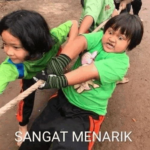a boy and a girl are playing tug of war with a rope on a dirt road .