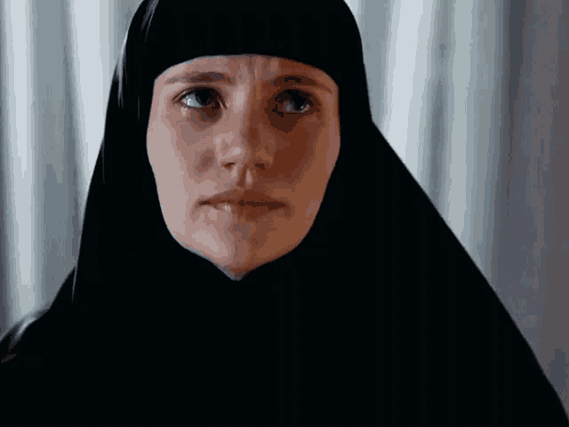 a woman wearing a black head scarf looks at the camera