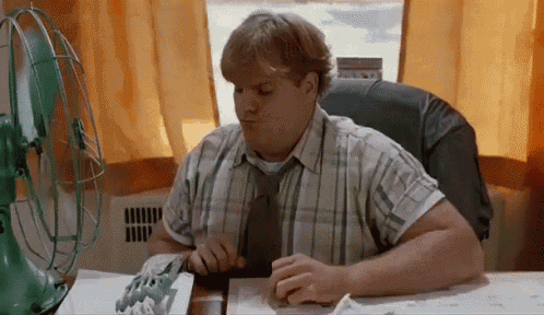 a man in a plaid shirt and tie is sitting at a desk in front of a green fan .