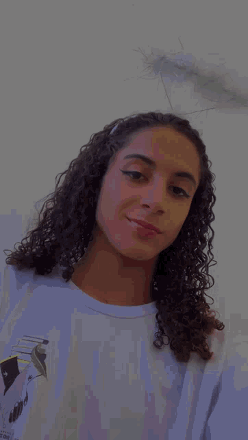 a young woman with curly hair is wearing a white shirt and a white feather halo on her head .