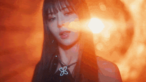 a close up of a woman 's face with a flower necklace in front of a fire background .