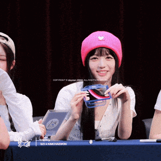 a girl wearing a pink hat with a heart on it is holding a phone