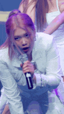 a woman in a white jacket is singing into a microphone and making a funny face