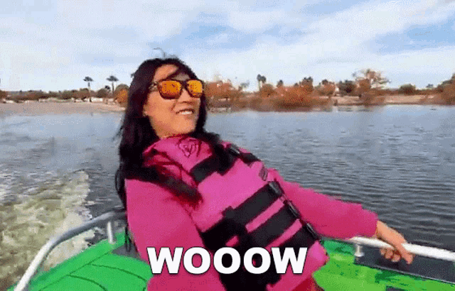 a woman wearing sunglasses and a life jacket is riding a boat with the word wooow written on it