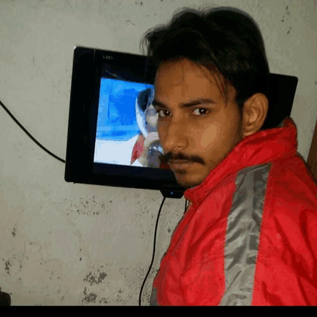 a man in a red jacket is standing in front of a tv screen
