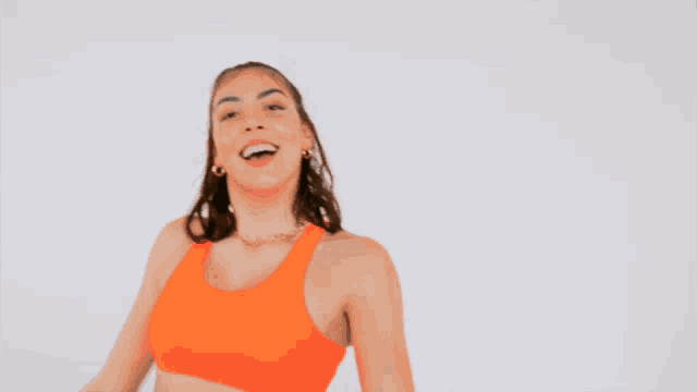 a woman in an orange tank top is dancing and her hair is blowing in the wind .