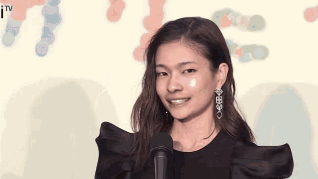 a woman wearing a black dress and earrings is talking into a microphone
