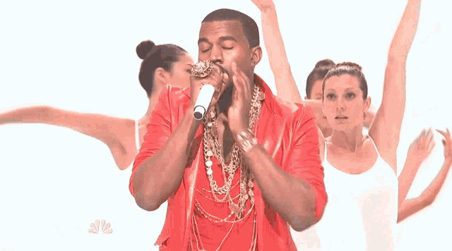 a man in a red jacket is singing into a microphone in front of a group of dancers