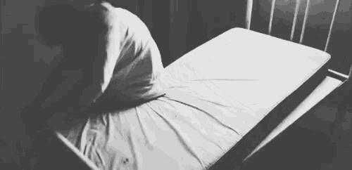 a black and white photo of a person standing next to a bed .