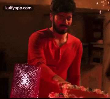 a man in a red shirt is cutting a cake in a room .