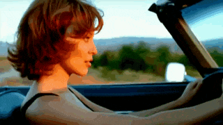 a woman with red hair is driving a car on a country road .