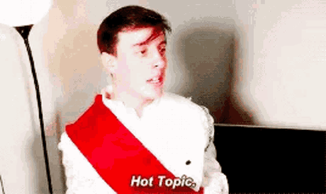 a young man wearing a red sash around his neck is talking to someone .