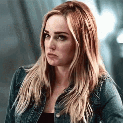 a woman with long blonde hair is wearing a denim jacket and making a sad face .