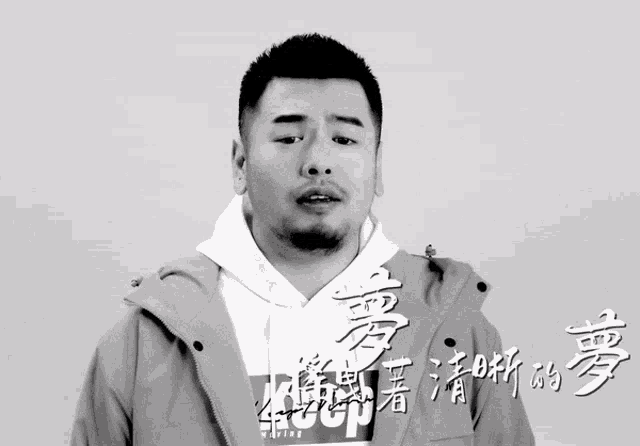 a man with a beard is wearing a white hoodie and a grey jacket
