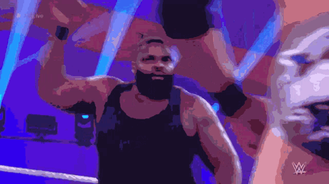 a man with a beard stands in a wrestling ring with the letters w on the bottom right