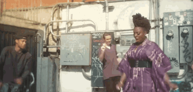 a woman in a purple dress is dancing in front of a wall with graffiti .