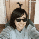 a woman wearing sunglasses and a ponytail is taking a selfie with her phone .