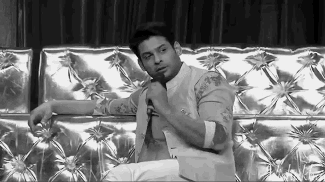 a black and white photo of a man sitting on a couch with his hand on his chin .