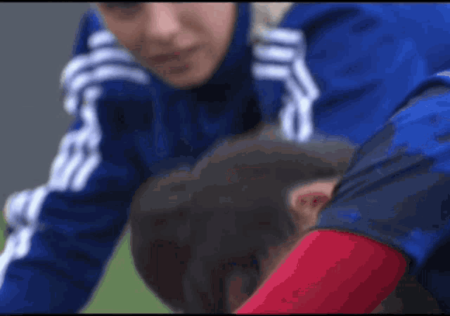 a man in a blue and white adidas jacket is laying on another man 's back