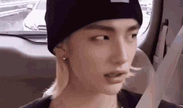 a young man wearing a black beanie and earrings is sitting in a car .