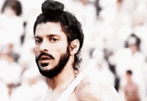 a man with a beard is wearing a white tank top and a bun .