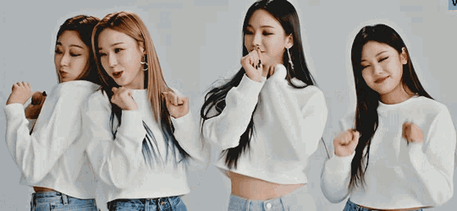 a group of young women wearing white sweaters and blue jeans are posing for a picture .