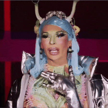 a drag queen wearing a blue wig and silver gloves is making a funny face