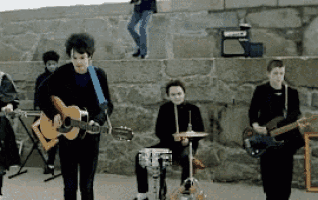 a group of people playing guitars and drums in front of a rock wall