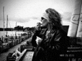 a black and white photo of a woman smoking a cigarette while looking out over a harbor .
