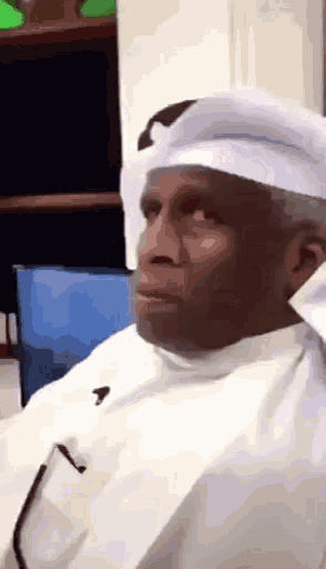a man wearing a white turban is sitting in a chair and making a funny face