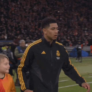 a man wearing a black jacket with yellow stripes is walking on a field