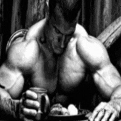 a very muscular man is sitting at a table eating food .
