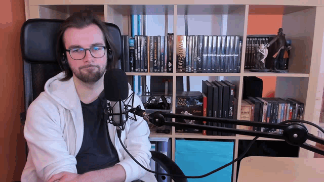 a man is sitting in front of a microphone with a bookshelf behind him that has twin peaks on it