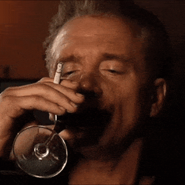 a man is smoking a cigarette while drinking a glass of wine