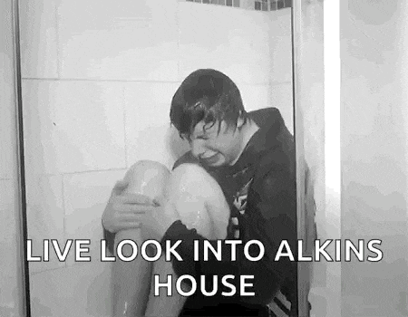 a man is kneeling in a shower with his legs in the water and the words `` live look into alkins house '' .