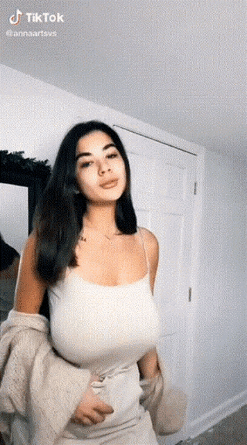 a woman with very large breasts is wearing a white tank top and a sweater .