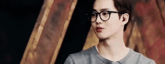 a young man wearing glasses and a gray shirt is looking at something .