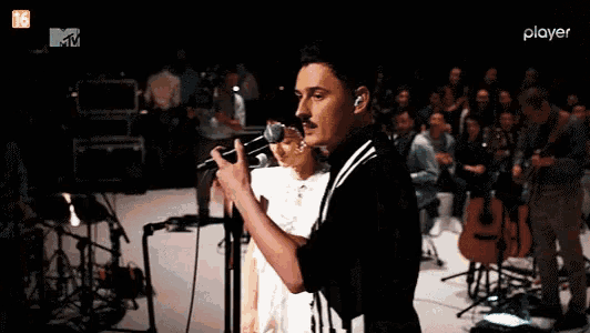 a man singing into a microphone in front of a player logo on a tv screen